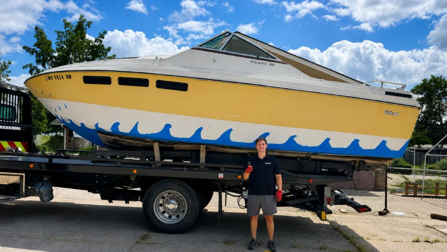 A Junk Pirates crew member next to a 1980s Wellcraft speedboat loaded onto our trailer for removal.