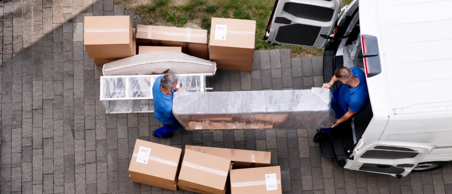 Aerial view of two Junk Pirates crew members loading a shrink-wrapped couch and moving boxes into a van.