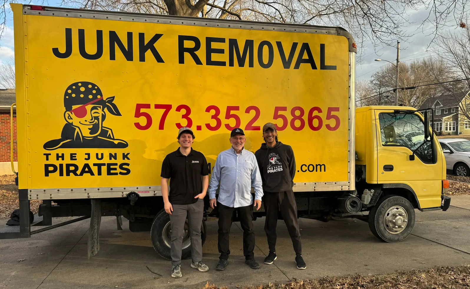 Ron Frost and the Junk Pirates crew standing in front of the company's yellow JUNK REMOVAL box truck in Columbia, MO.