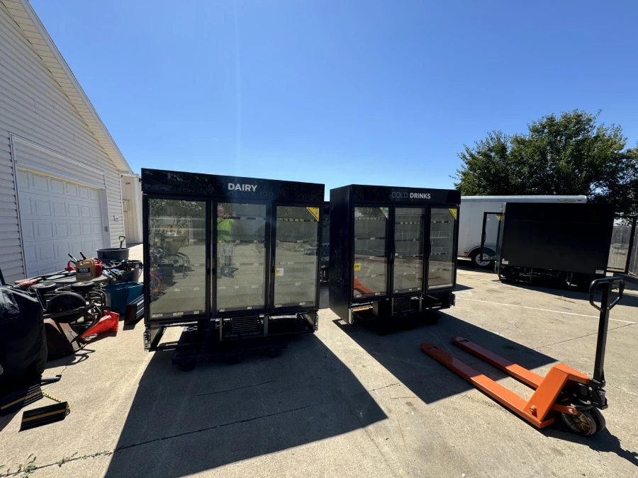 The donated Dairy and Cold Drinks display coolers staged on pallets next to a pallet jack, waiting to be loaded onto the Food Bank truck.