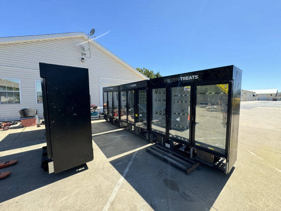 Five of the donated commercial glass-door units lined up on pallets in the yard, labelled Frozen Treats and Fresh Foods, ready for pickup.