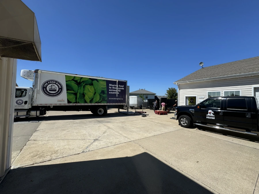 A refrigerated Food Bank for Central and Northeast Missouri box truck backed up at the Junk Pirates yard in Columbia, MO, with a Junk Pirates truck parked alongside and the crew loading donated refrigeration units.