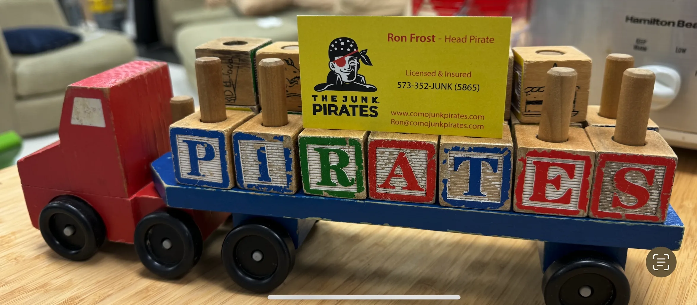 A small wooden toy truck spelling PIRATES with a business card reading Ron Frost — Head Pirate, Licensed & Insured.