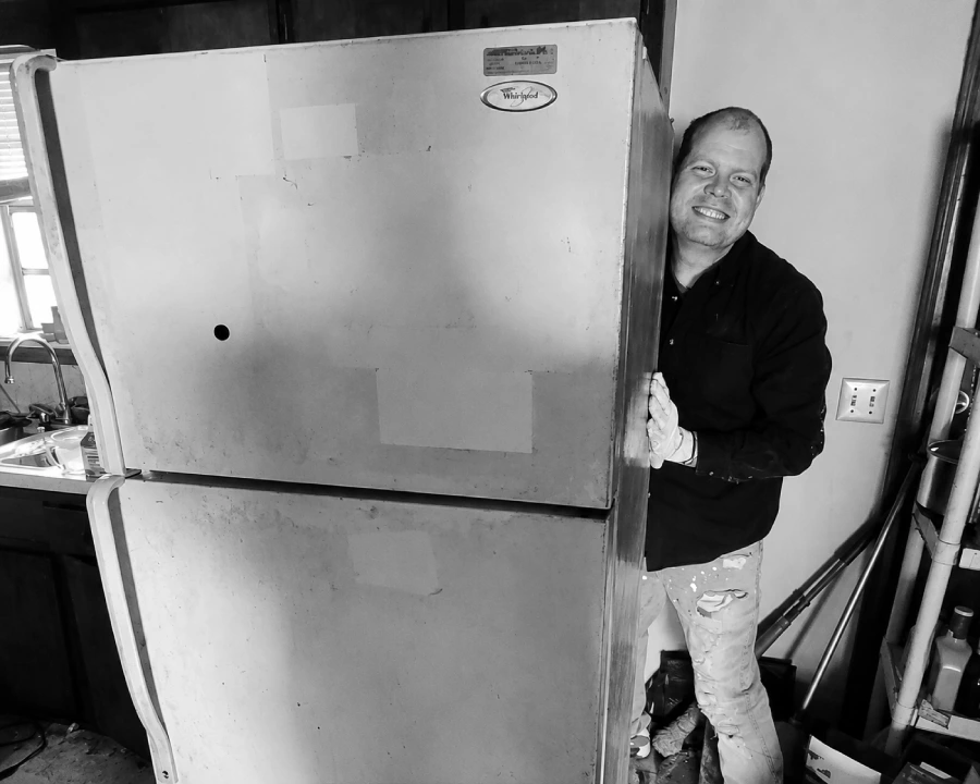 A Junk Pirates crew member smiling next to a Whirlpool refrigerator pulled from a kitchen.