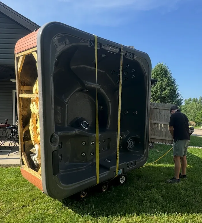 A Junk Pirates crew member rigging a six-person hot tub on its side in a Columbia, MO backyard, ready to roll out for removal.