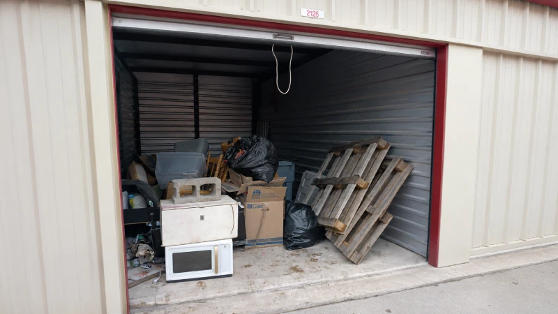 A 10 by 20 storage unit in Columbia, MO packed with a microwave, pallets, cardboard boxes, trash bags, and miscellaneous household junk before pickup.