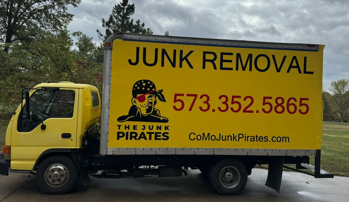 The Junk Pirates branded yellow box truck — JUNK REMOVAL, 573-352-5865 — on a rural road outside Columbia, MO.